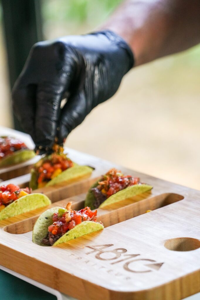 Chef ganté garnissant des mini-tacos sur une planche 4810 Traiteur