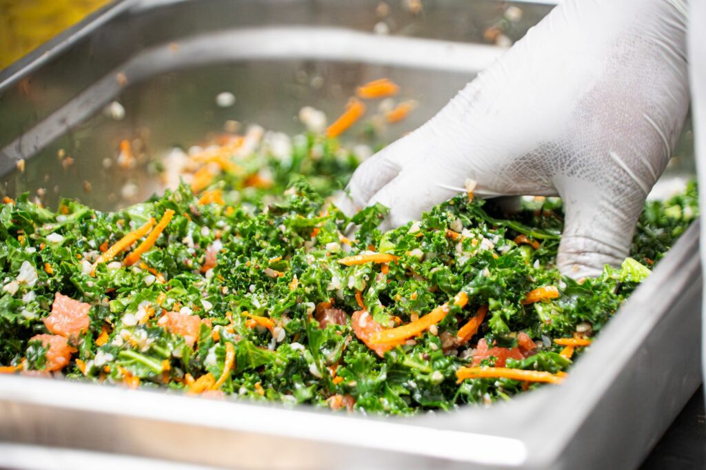 Main gantée mélangeant une salade d’herbes fraîches et de carottes