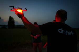 Technicien tenant à bout de bras un drone allumé en rouge à la tombée de la nuit