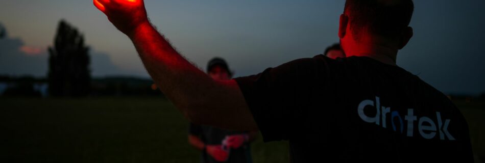 Technicien tenant à bout de bras un drone allumé en rouge à la tombée de la nuit